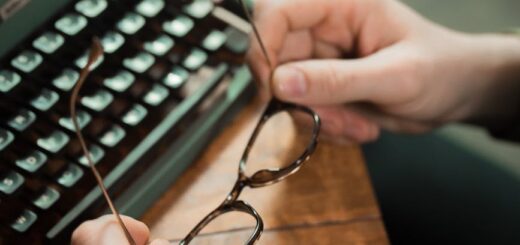 person holding an eyeglasses near a vintage typewriter